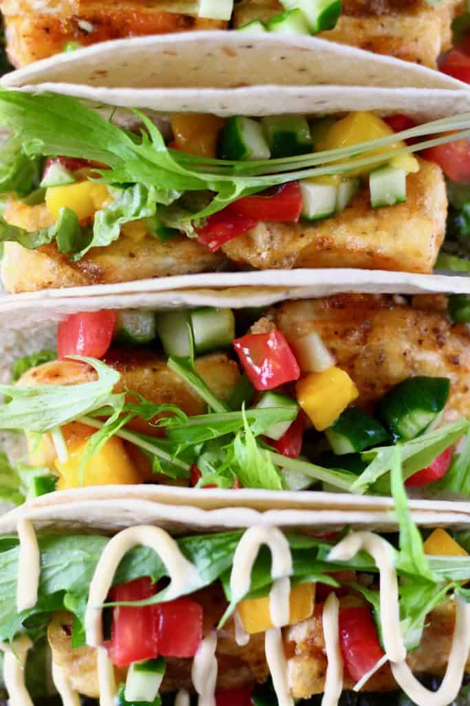 Photo of four tortillas stuffed with crispy tofu, mango, tomato, cucumber and lettuce on a blue plate
