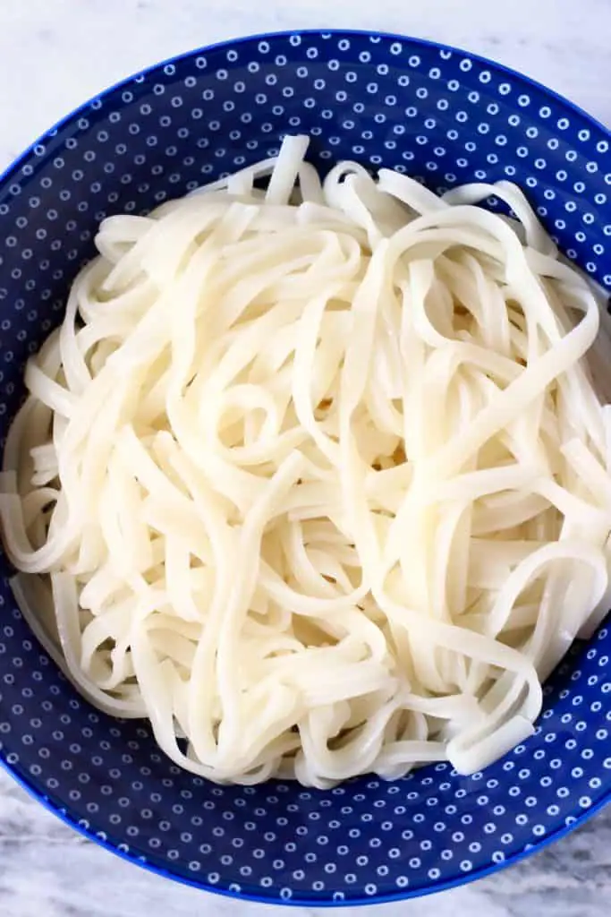 A blue bowl filled with cooked rice noodles against a marble background