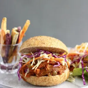 A vegan eggplant pulled pork burger with coleslaw and sweet potato fries and salad in the background