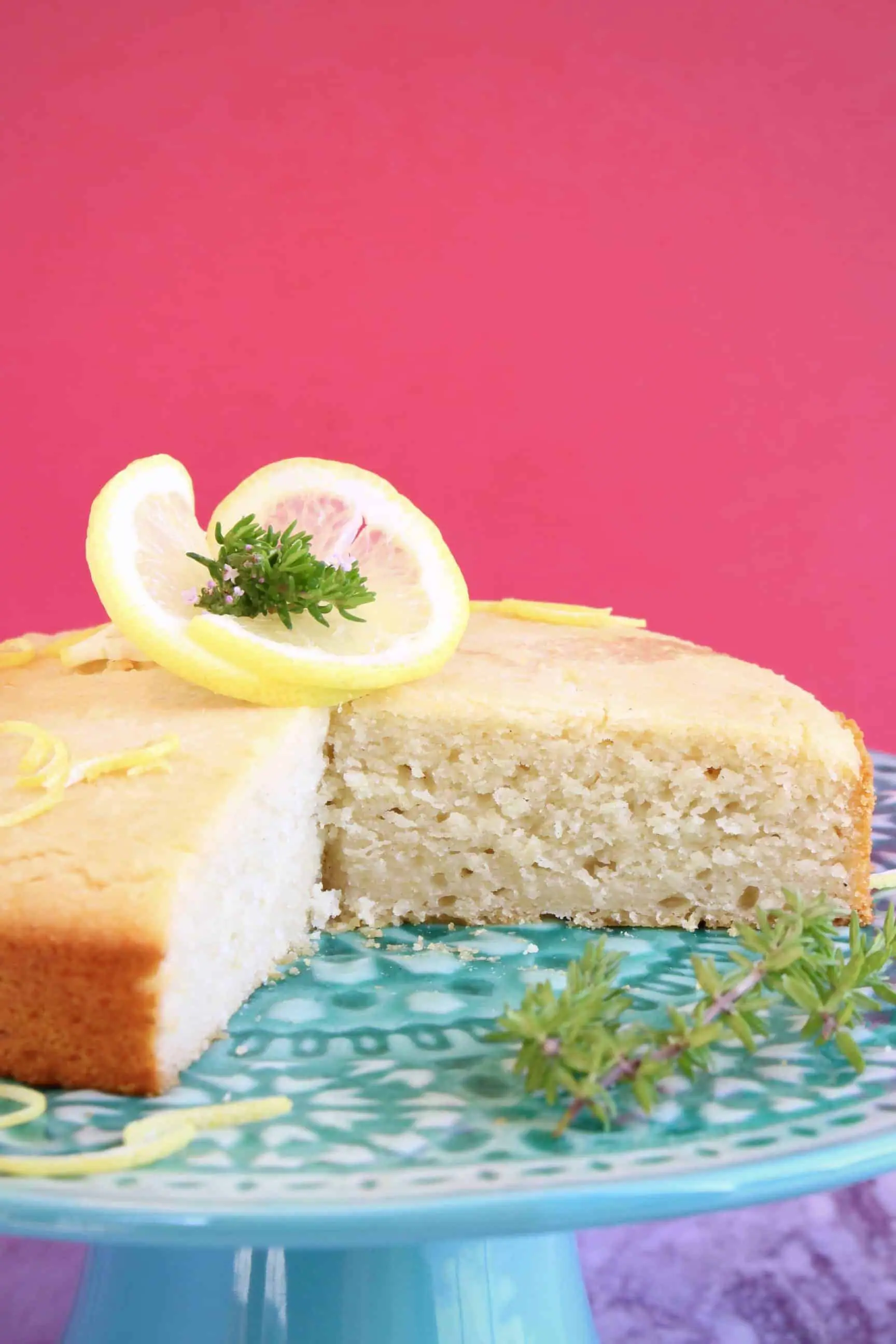 Gluten-free vegan lemon drizzle cake with a slice taken out of it on a cake stand 