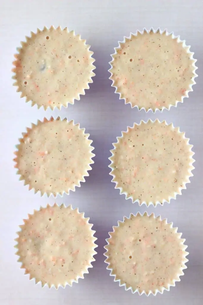 Six cupcake cases filled with raw carrot cake batter against a white background