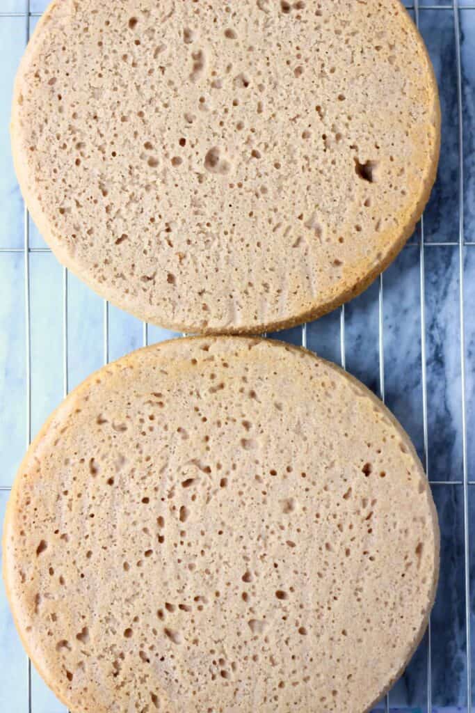 Photo of two brown sponge cakes on a wire rack against a marble background