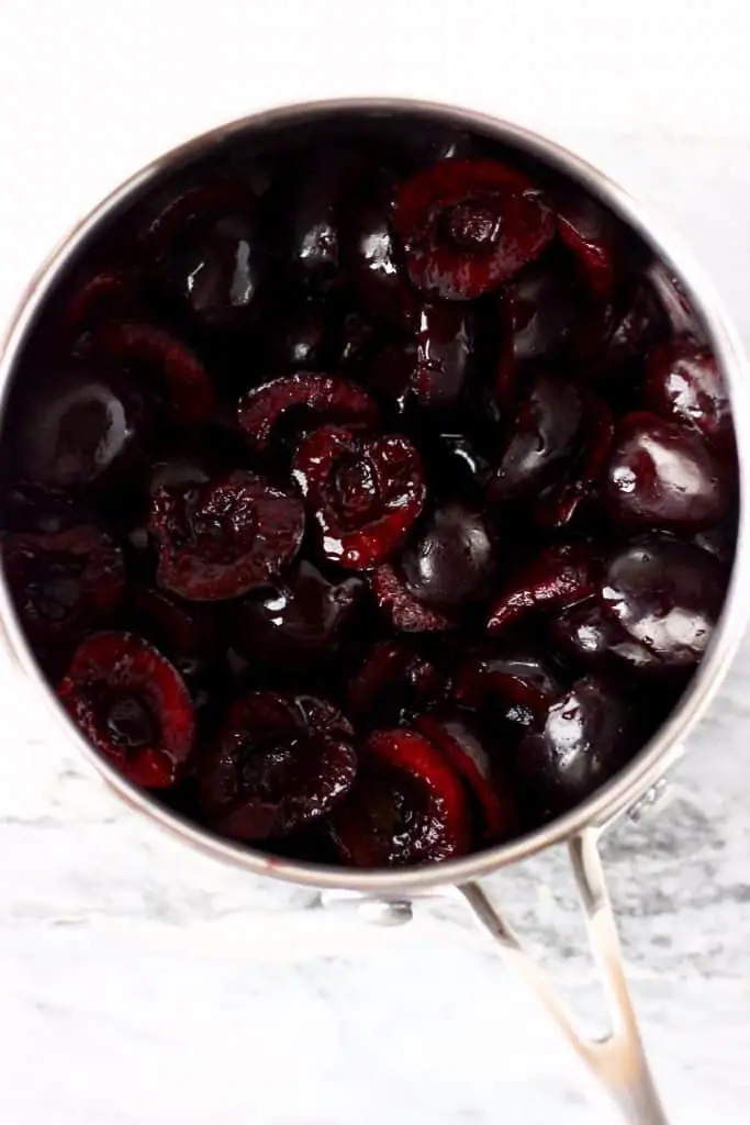 Pitted cherry halves in a silver saucepan against a marble background
