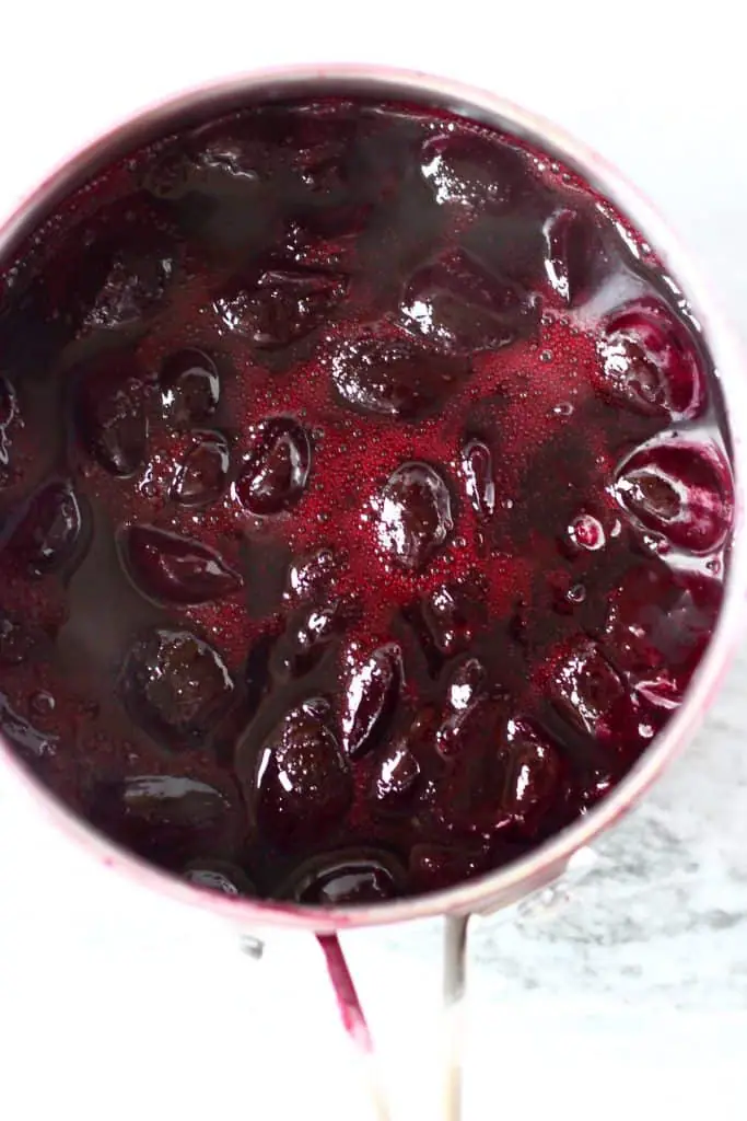 Cooked cherries in a silver saucepan against a marble background