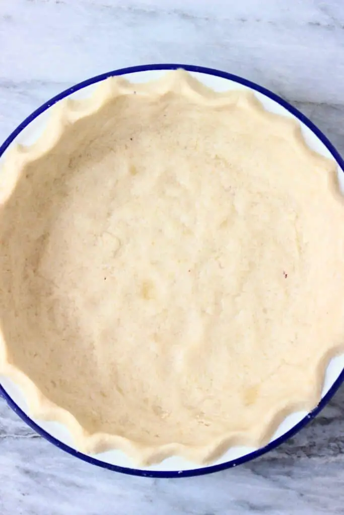 Raw pie crust in a white pie dish with a blue rim against a marble background
