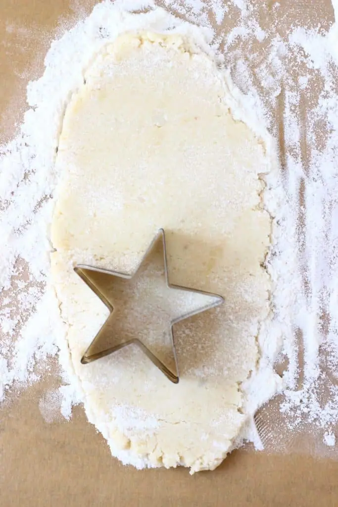 Pastry dough rolled out on a piece of brown baking paper with a silver star-shaped cookie cutter cutting out star shapes
