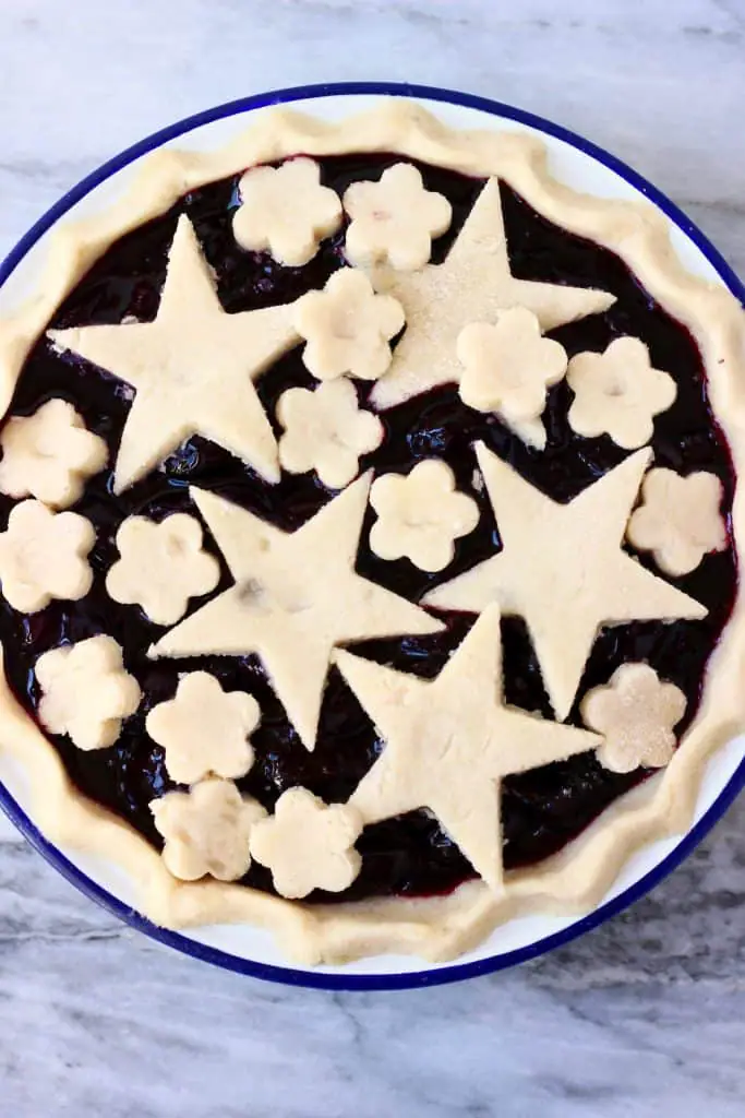 Raw cherry pie topped with stars and flowers in a white pie dish with a blue rim against a marble background