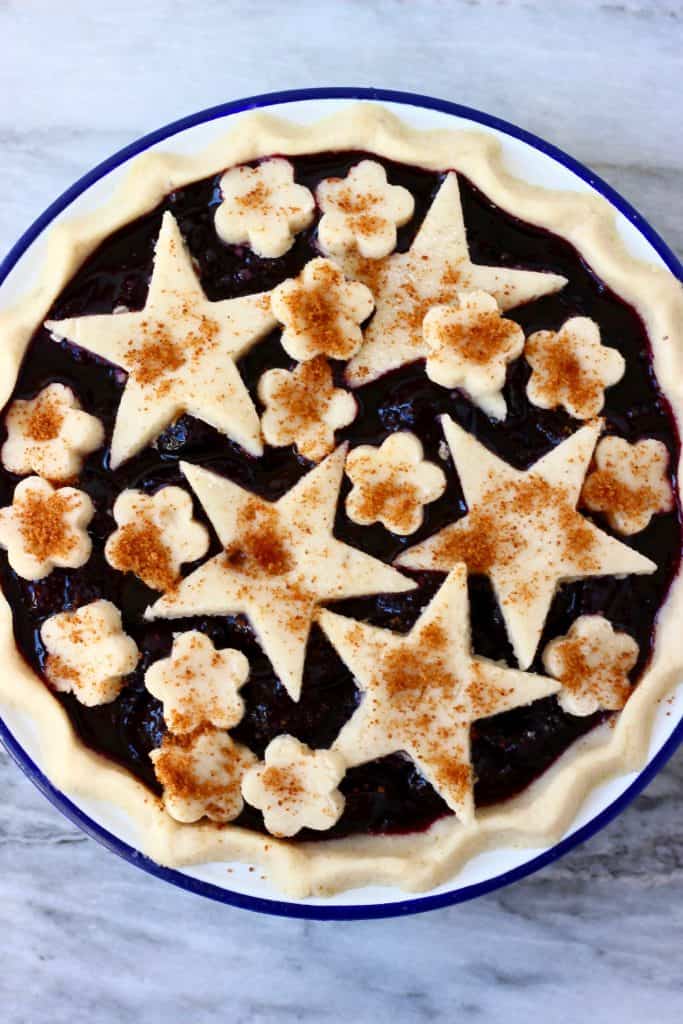 Cherry pie topped with stars and flowers in a white pie dish with a blue rim against a marble background