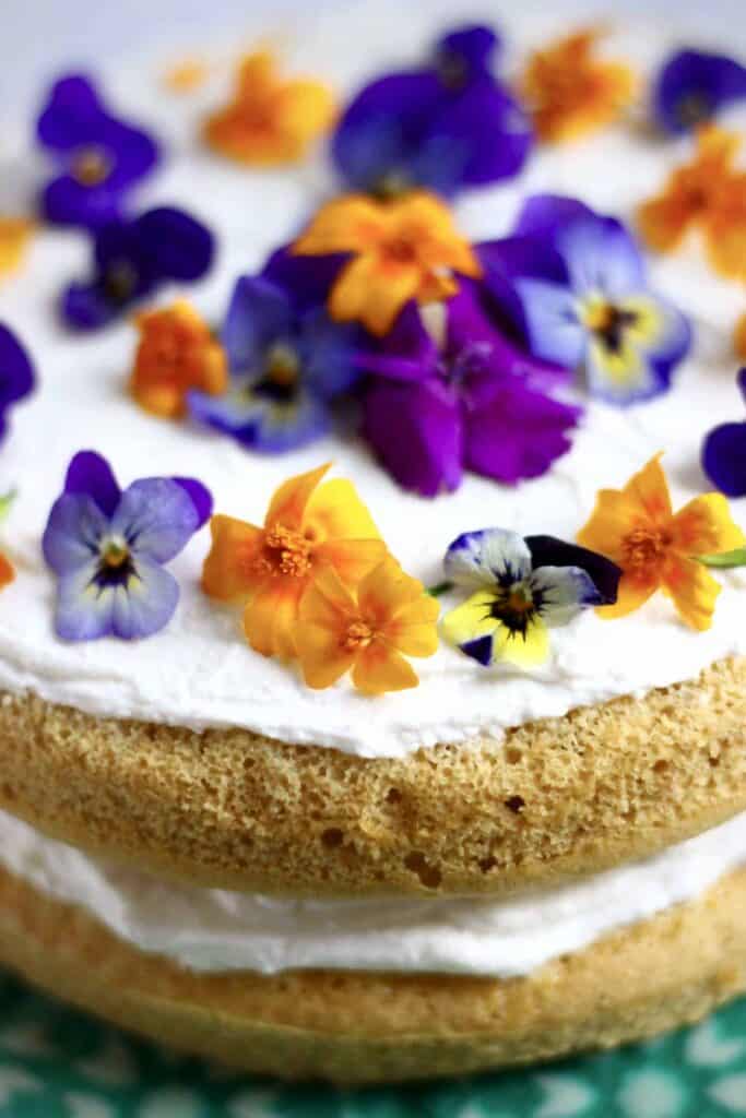 Photo of orange sponge cake sandwiched with white creamy frosting topped with purple and orange flowers