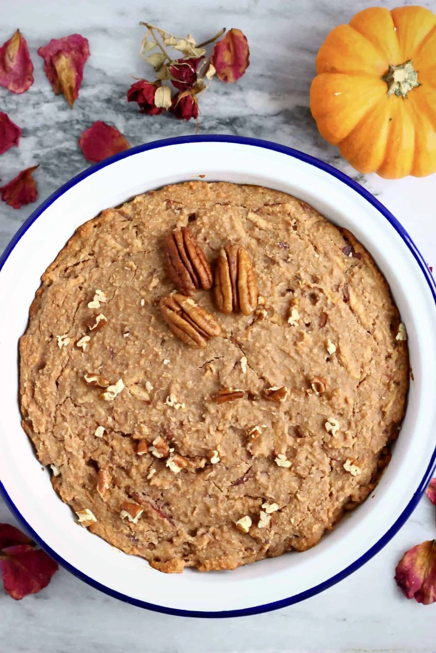 A gluten-free vegan apple cake in a round baking dish topped with chopped pecan nuts