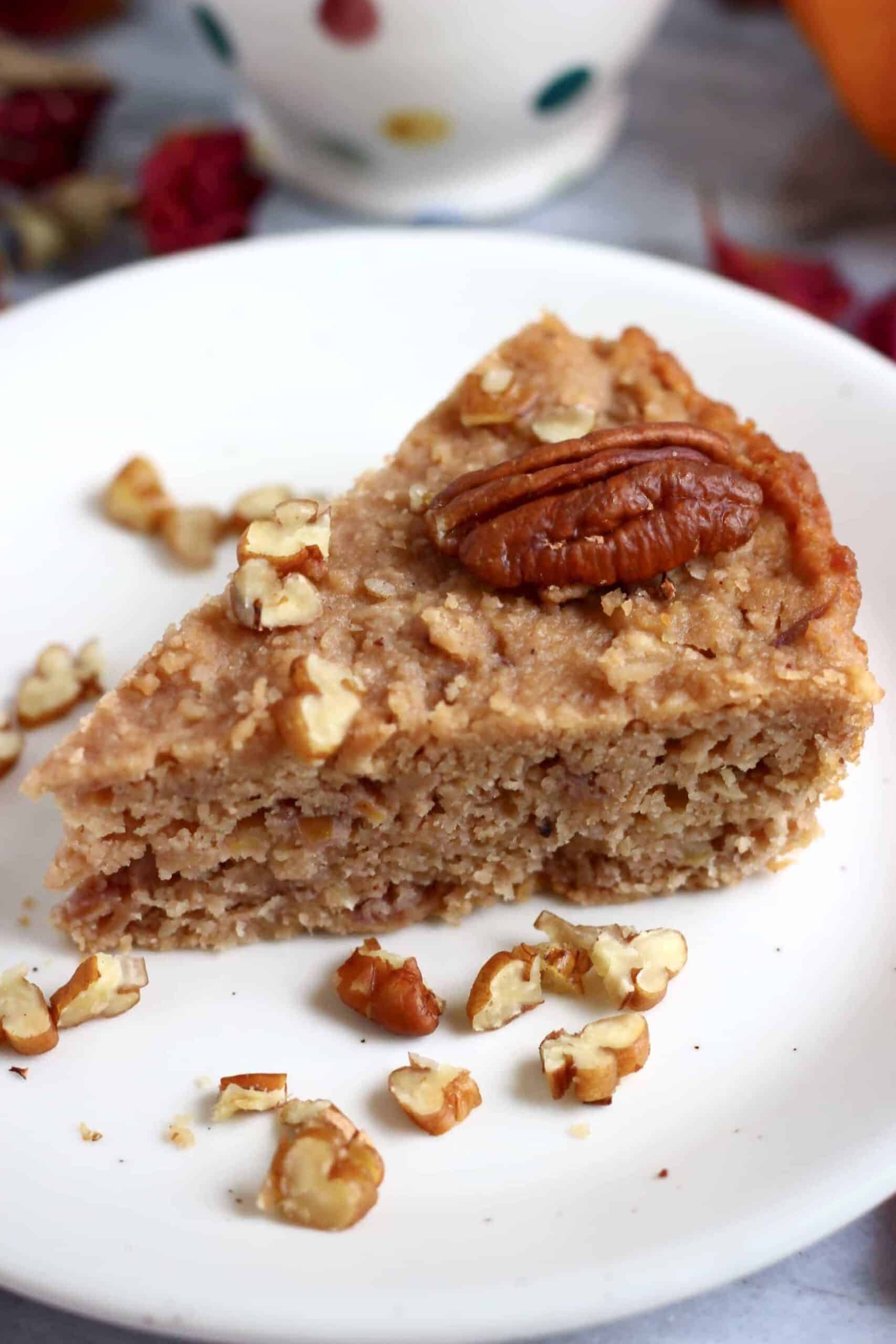 A slice of gluten-free vegan apple cake on a plate topped with a pecan nut 
