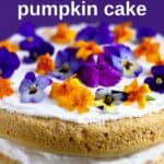 Photo of a sponge cake topped with flowers on a blue cake stand with a purple background