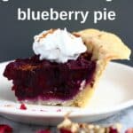 Photo of a slice of blueberry pie topped with cream on a white plate and a grey background