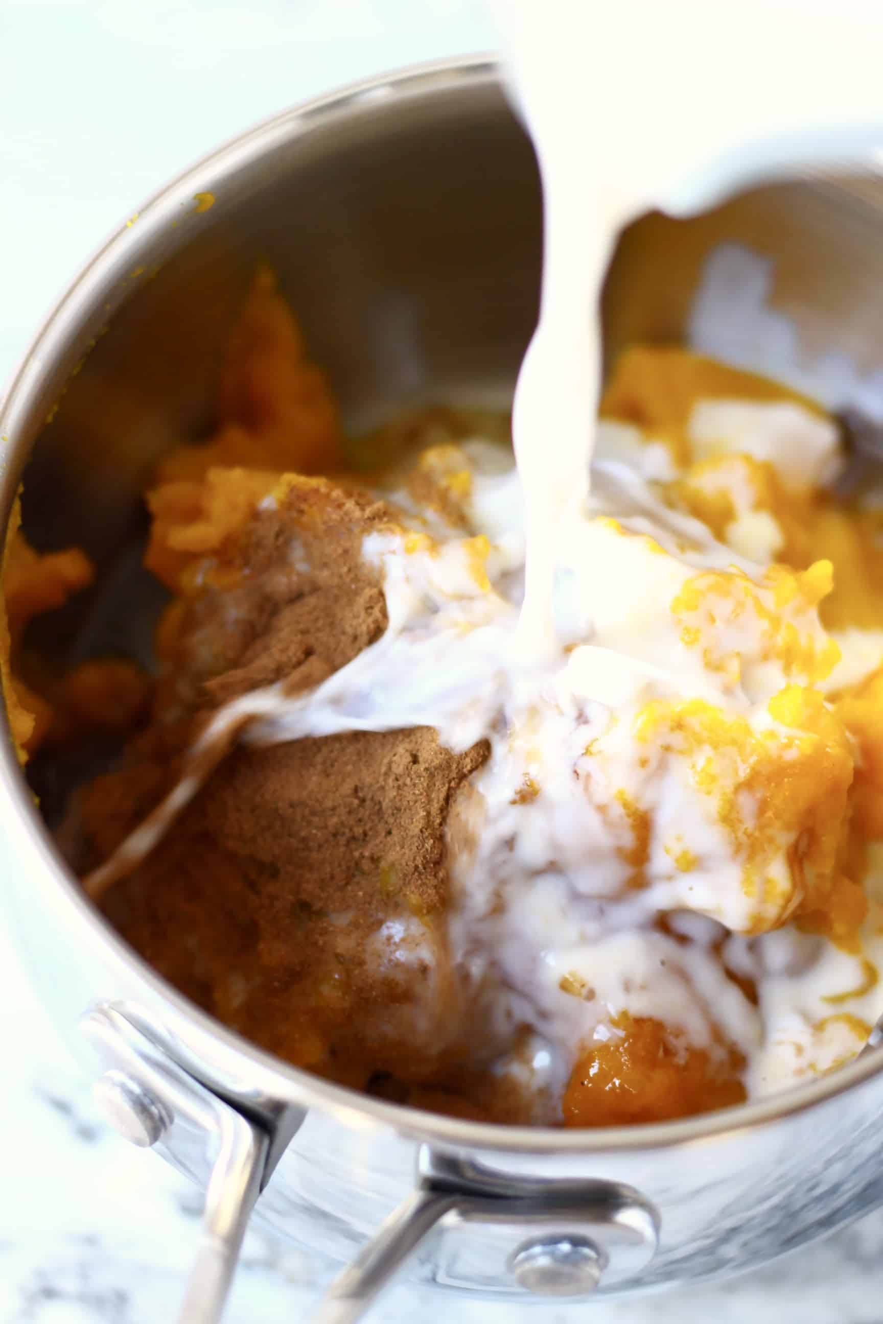 This Gluten-Free Vegan Pumpkin Pie is perfectly spiced, rich and creamy, and flaky, crispy and buttery. The perfect dessert for autumn/fall, Thanksgiving and Christmas. Egg-free, dairy-free and refined sugar free. #vegan #rhiansrecipes #dairyfree #glutenfree #pie #pumpkin #thanksgiving Pumpkin purée and spices in a saucepan with milk being poured in with a jug