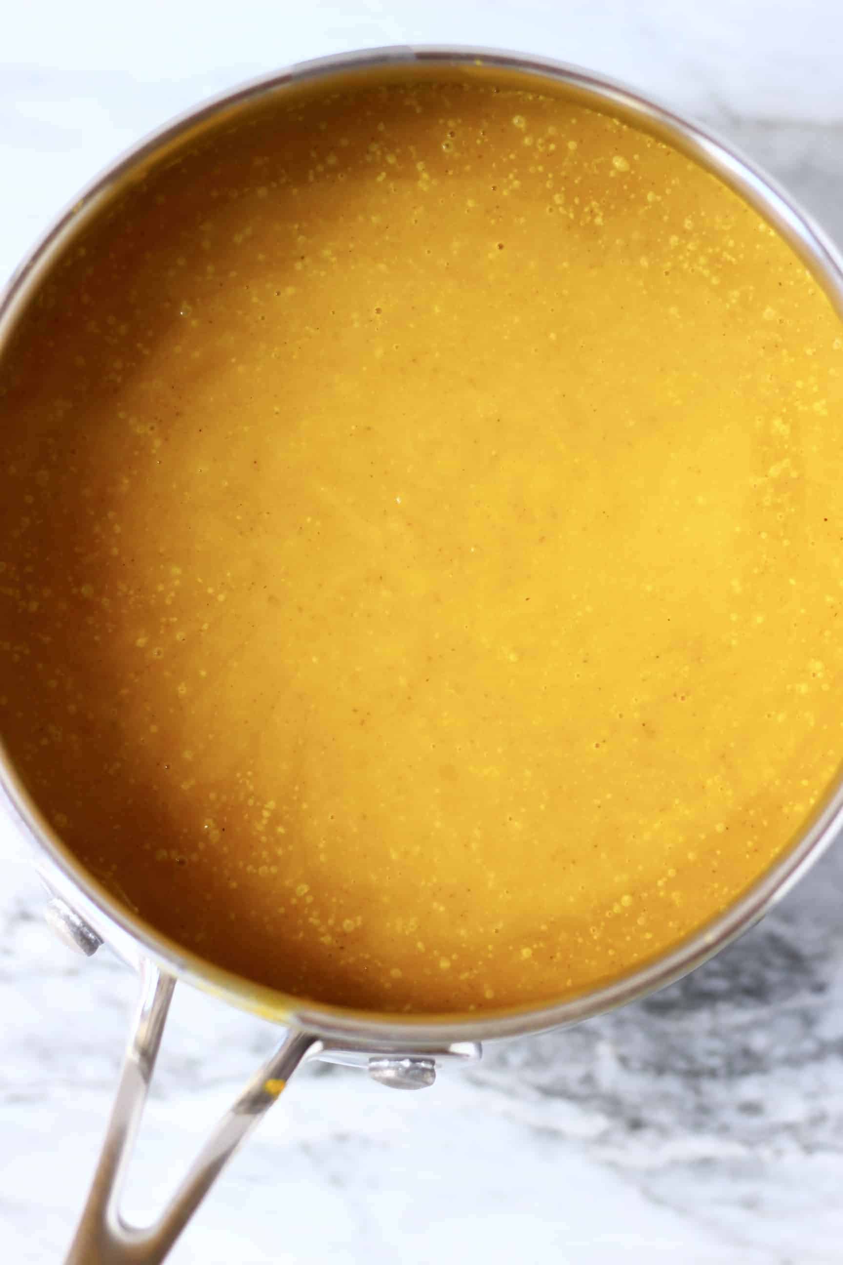 This Gluten-Free Vegan Pumpkin Pie is perfectly spiced, rich and creamy, and flaky, crispy and buttery. The perfect dessert for autumn/fall, Thanksgiving and Christmas. Egg-free, dairy-free and refined sugar free. #vegan #rhiansrecipes #dairyfree #glutenfree #pie #pumpkin #thanksgiving Dark orange gluten-free vegan pumpkin pie filling in a saucepan