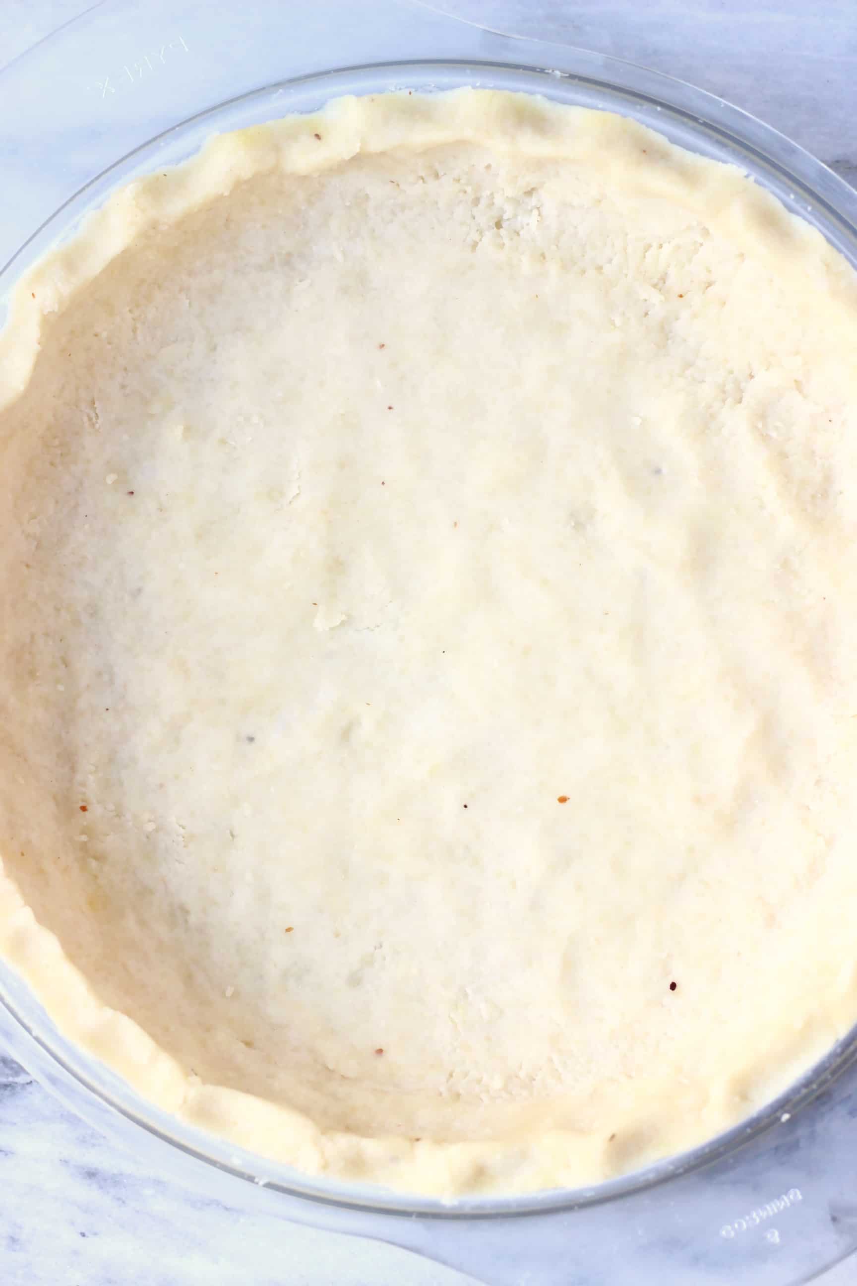 A raw gluten-free vegan pie crust in a glass pie dish against a marble background