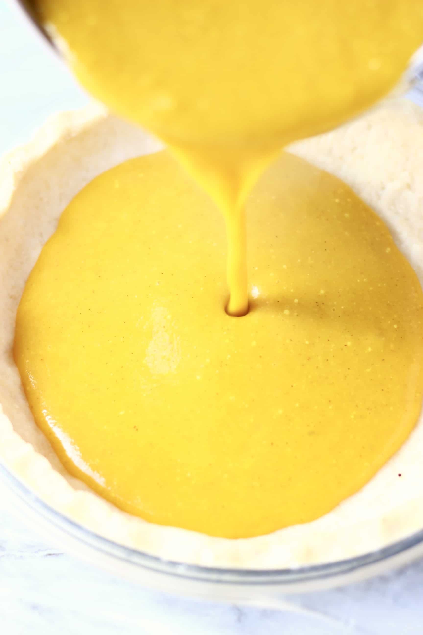 A raw gluten-free vegan pumpkin pie crust with orange pumpkin pie filling being poured in from a saucepan