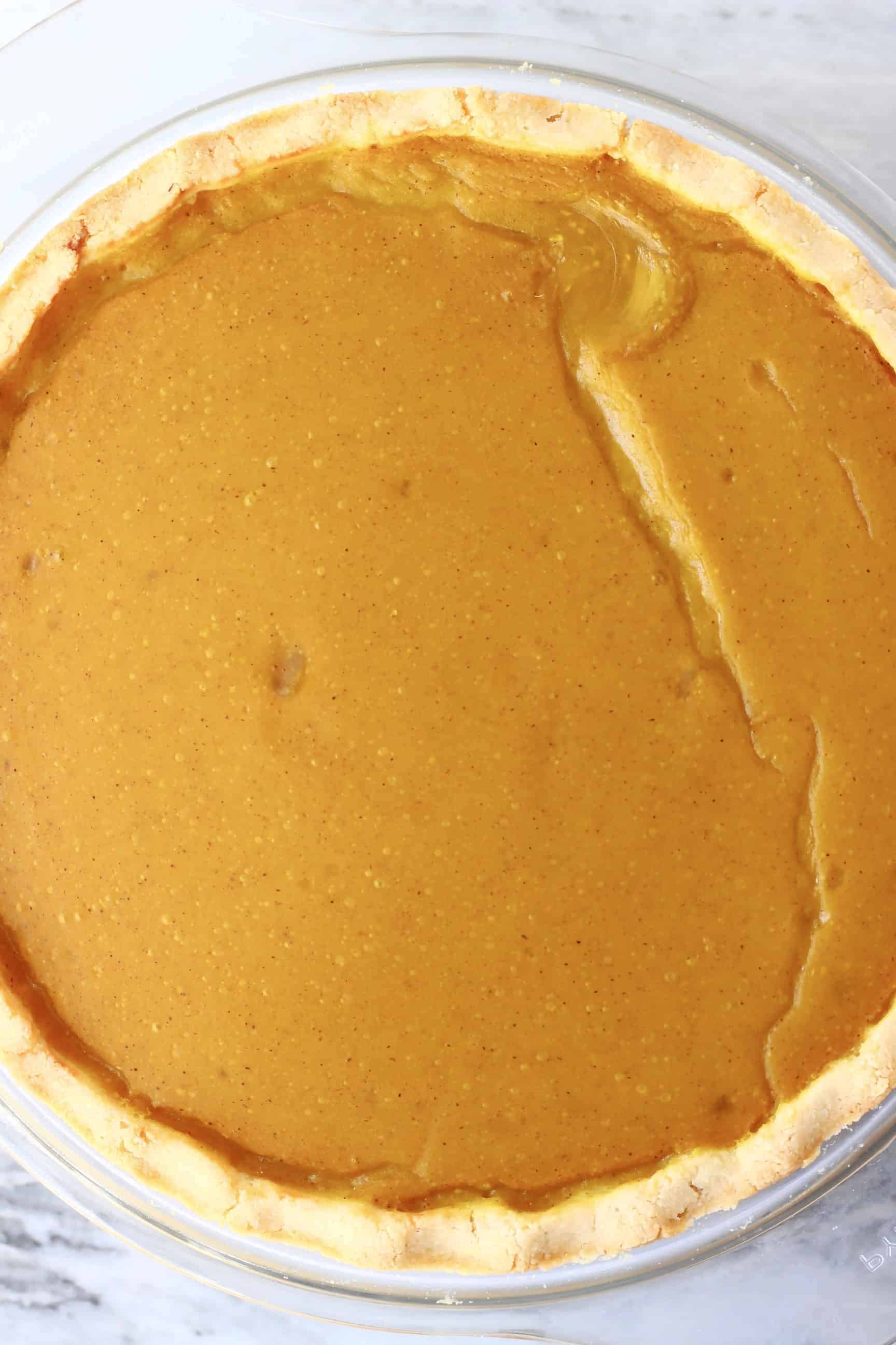 This Gluten-Free Vegan Pumpkin Pie is perfectly spiced, rich and creamy, and flaky, crispy and buttery. The perfect dessert for autumn/fall, Thanksgiving and Christmas. Egg-free, dairy-free and refined sugar free. #vegan #rhiansrecipes #dairyfree #glutenfree #pie #pumpkin #thanksgiving A cooked gluten-free vegan pumpkin pie in a glass pie dish