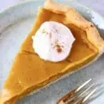 A slice of gluten-free vegan pumpkin pie topped with cream on a plate with a fork