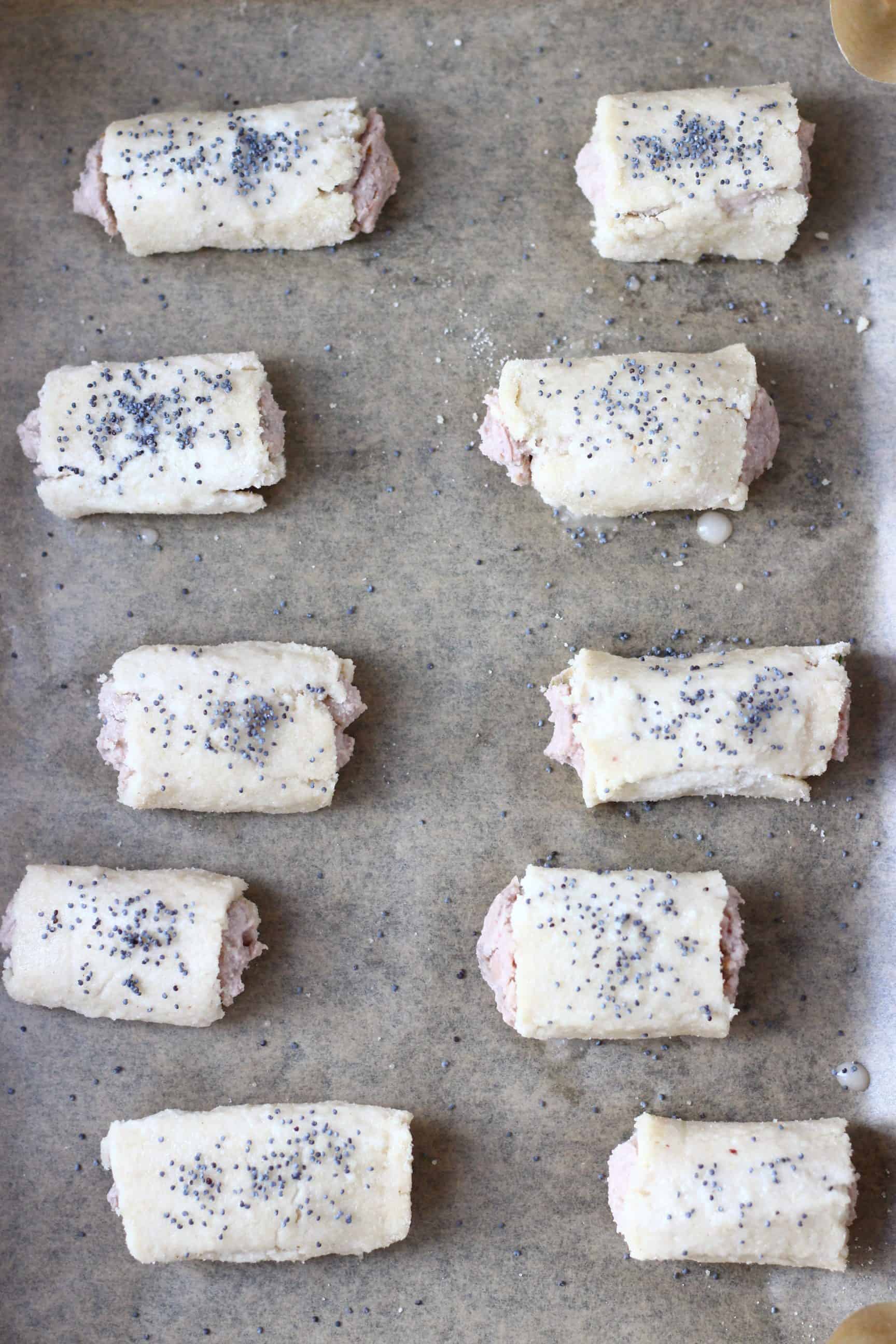 Ten uncooked vegan sausage rolls sprinkled with poppy seeds on a baking tray