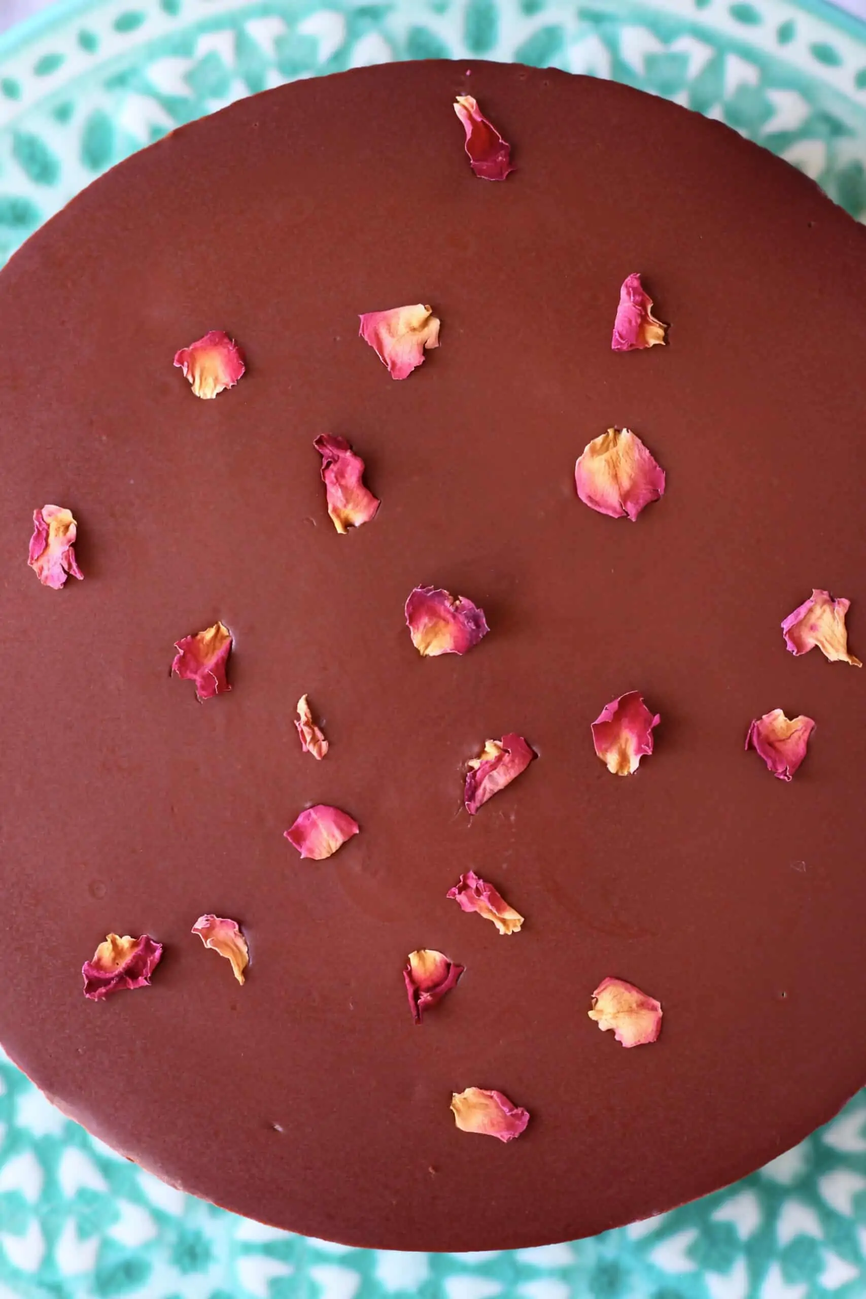 A gluten-free vegan chocolate mousse cake topped with vegan ganache and decorated with rose petals