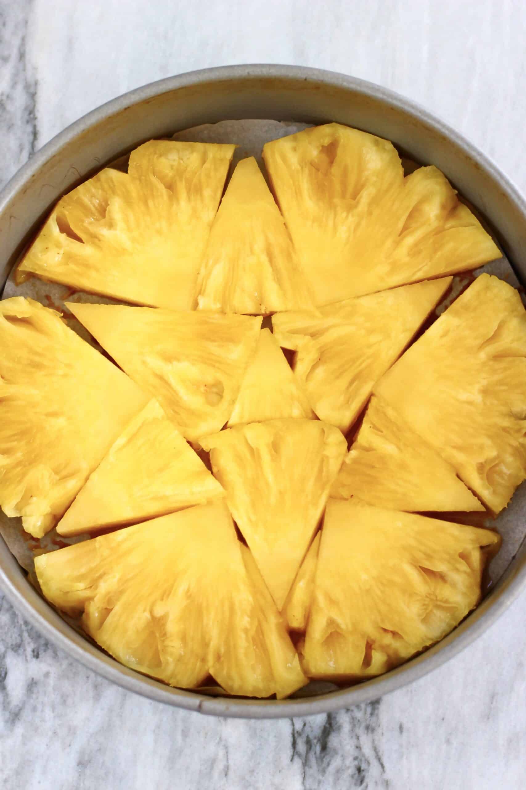 Pineapple chunks laid out on the bottom of a round springform baking tin lined with baking paper