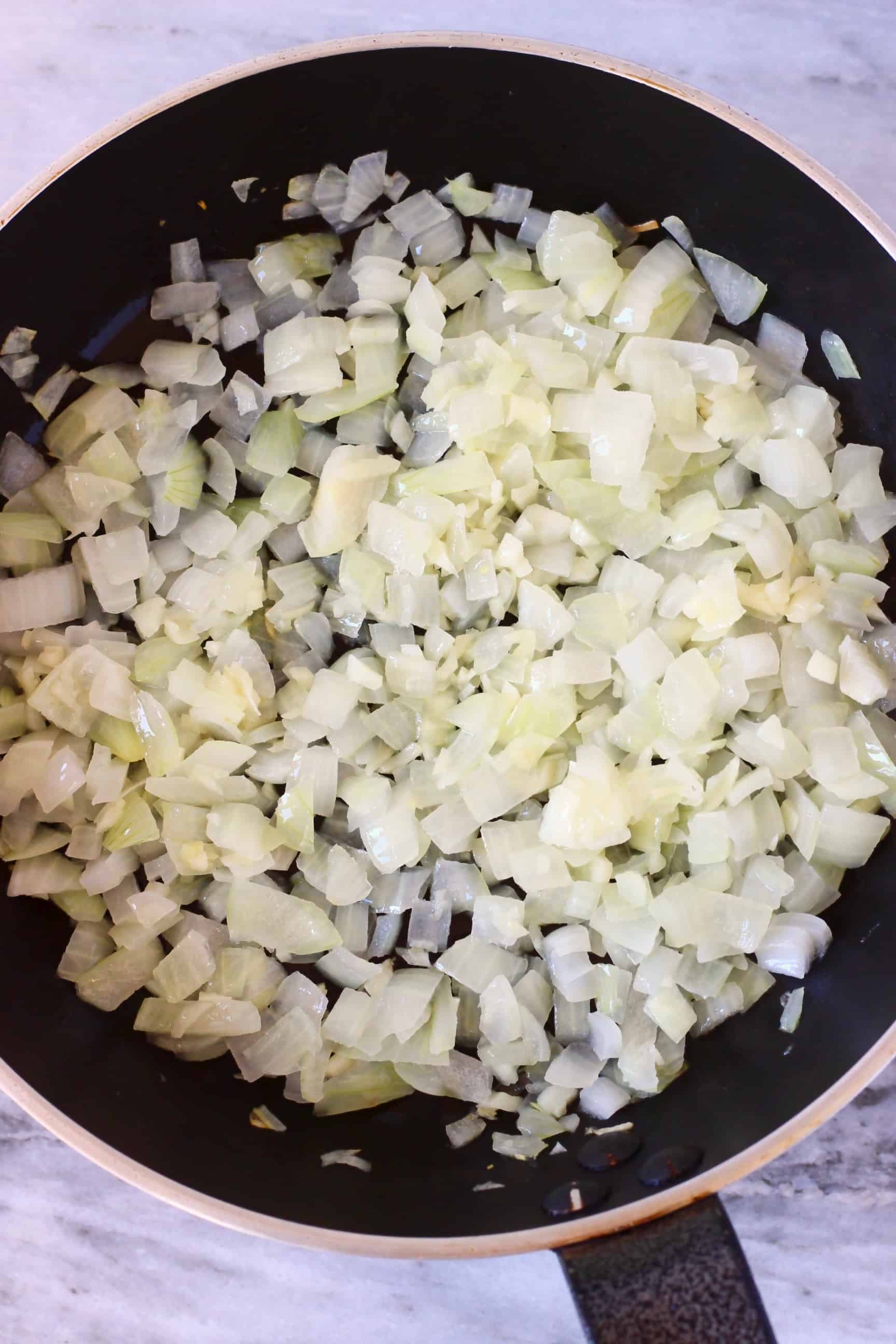 Diced onions being fried in a black frying pan