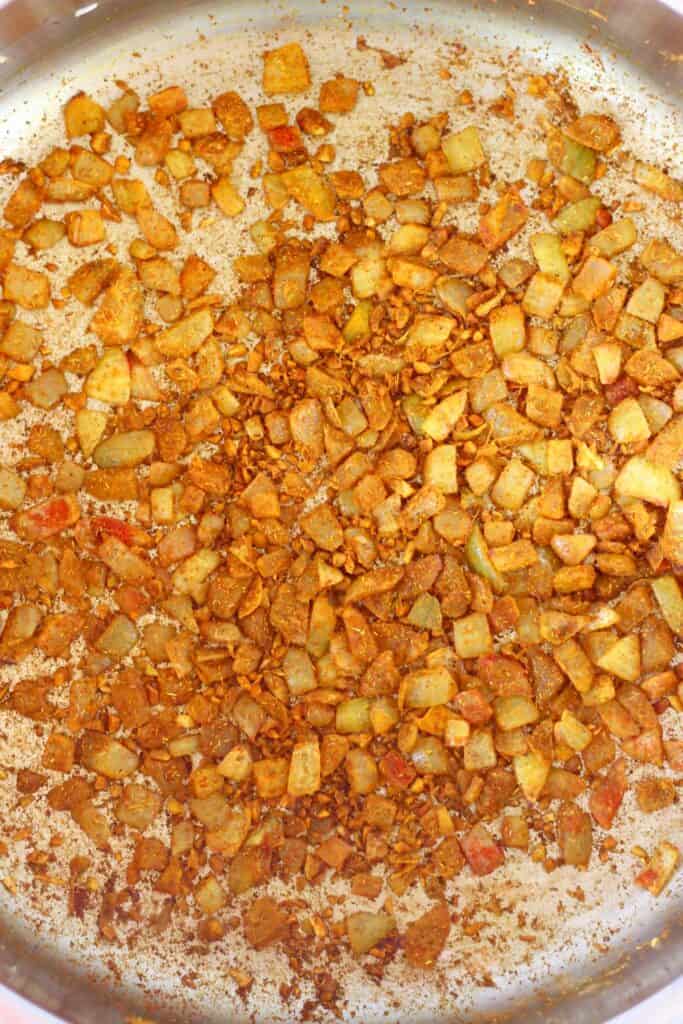 Photo of diced onion with brown spices being fried in a silver saucepan