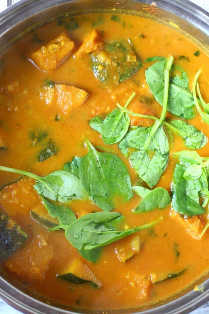 Photo of diced pumpkin, chickpeas and spinach in a yellow curry sauce in a silver saucepan