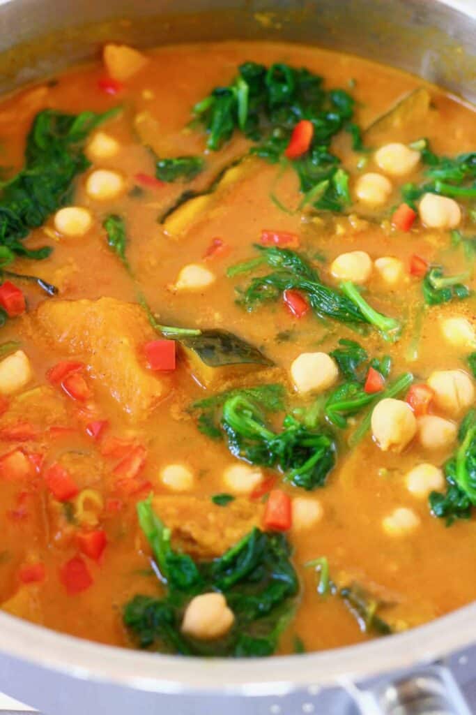 Photo of diced pumpkin, chickpeas and spinach in a yellow curry sauce in a silver saucepan