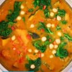Photo of orange curry with diced pumpkin, chickpeas and spinach in a silver saucepan