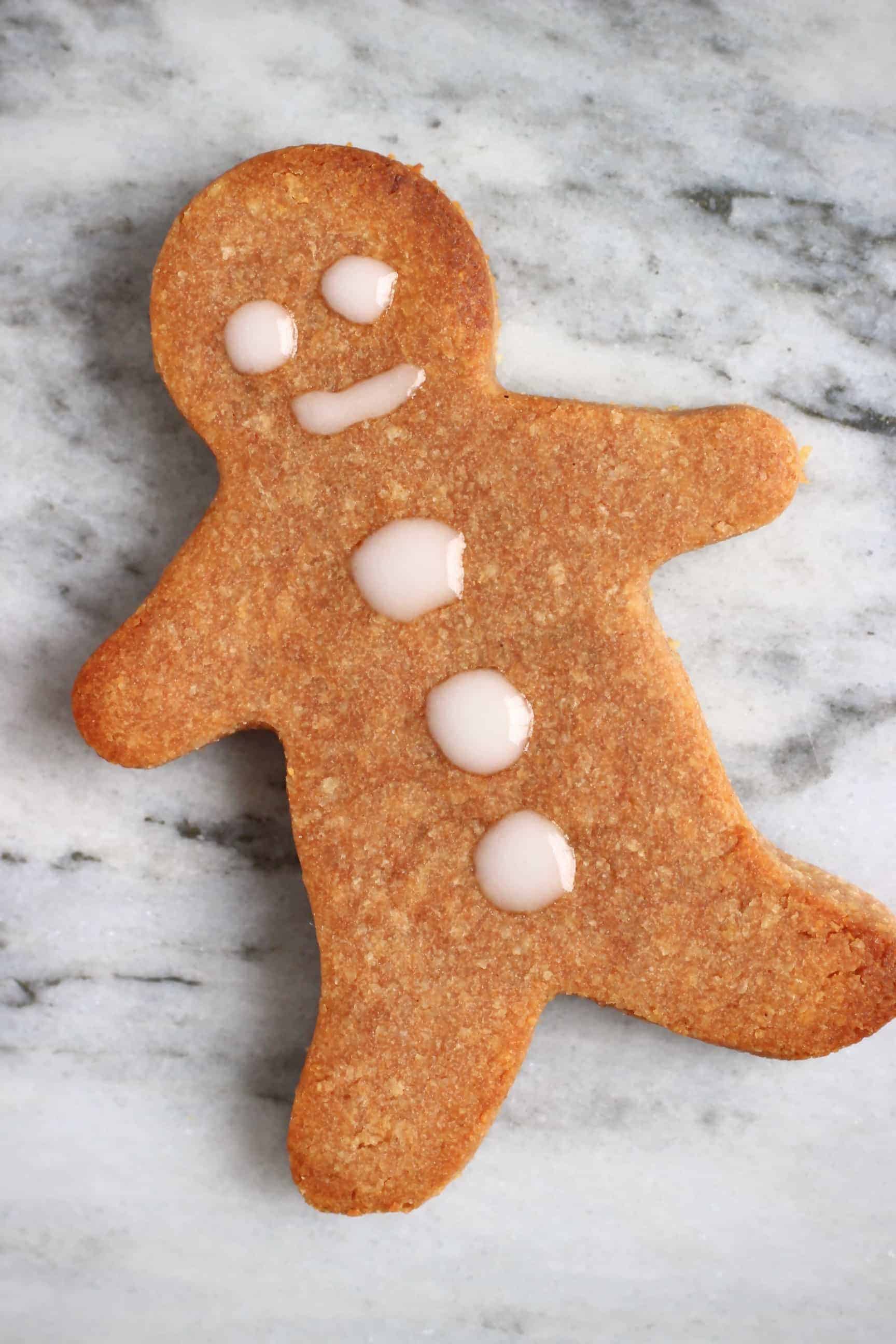 A gluten-free vegan gingerbread man cookie with an icing face against a marble background