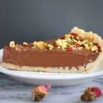 A slice of gluten-free vegan chocolate tart topped with chopped pistachios and freeze-dried raspberries
