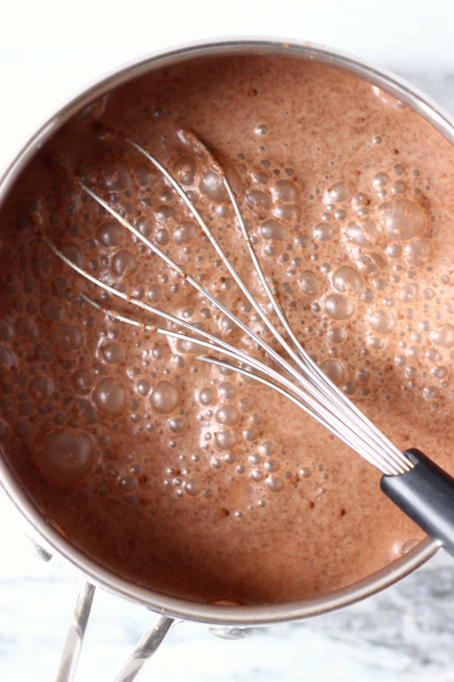 Vegan chocolate custard being made in a pan with a whisk