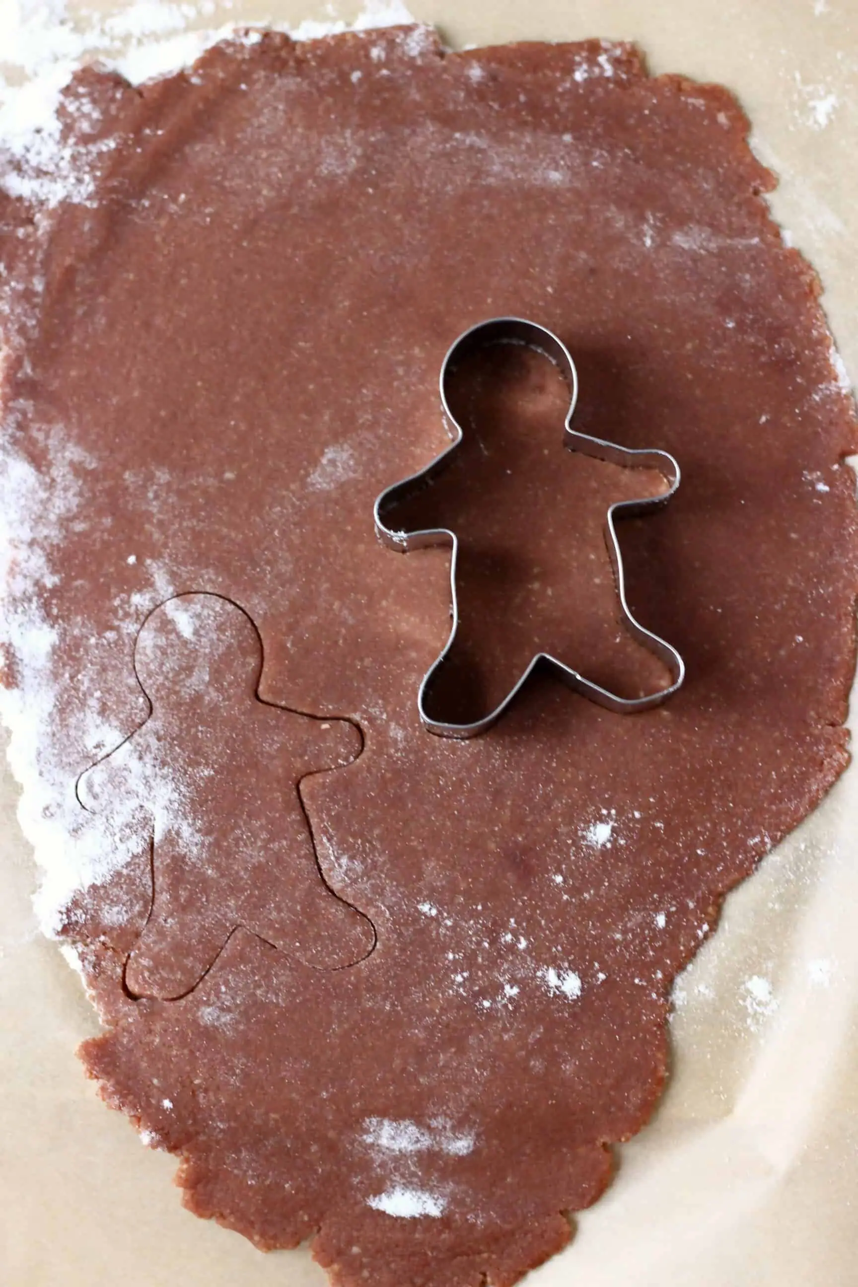 Raw gluten-free vegan gingerbread cookie dough on a sheet of baking paper with a silver gingerbread man cookie cutter 
