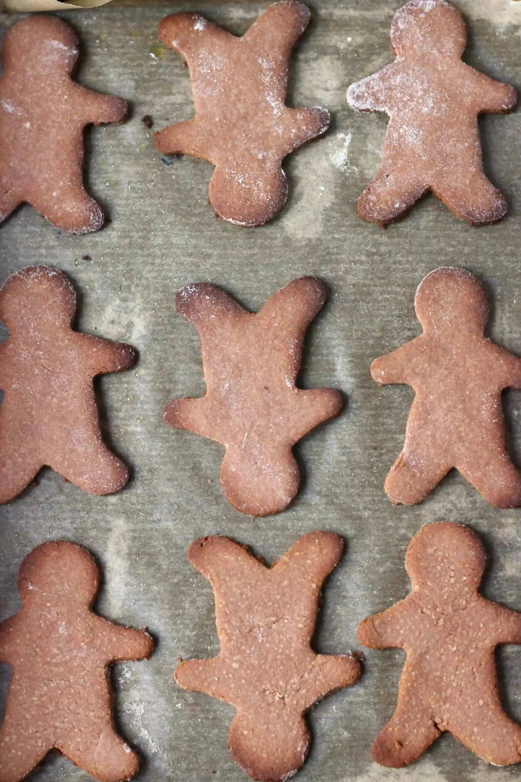 Nine baked gluten-free vegan gingerbread cookies on a sheet of baking paper