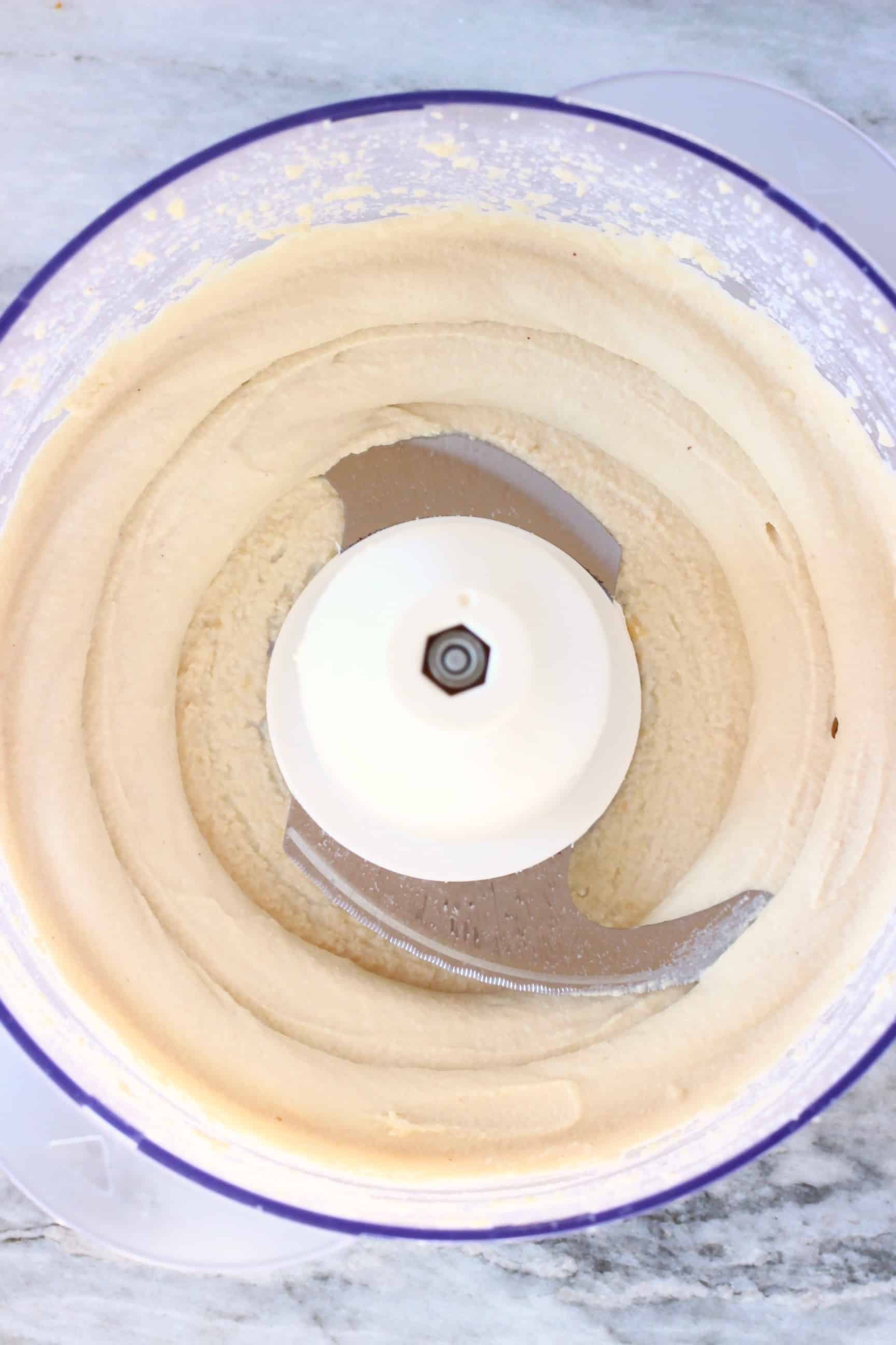 White vegan cashew buttercream in a food processor against a marble background