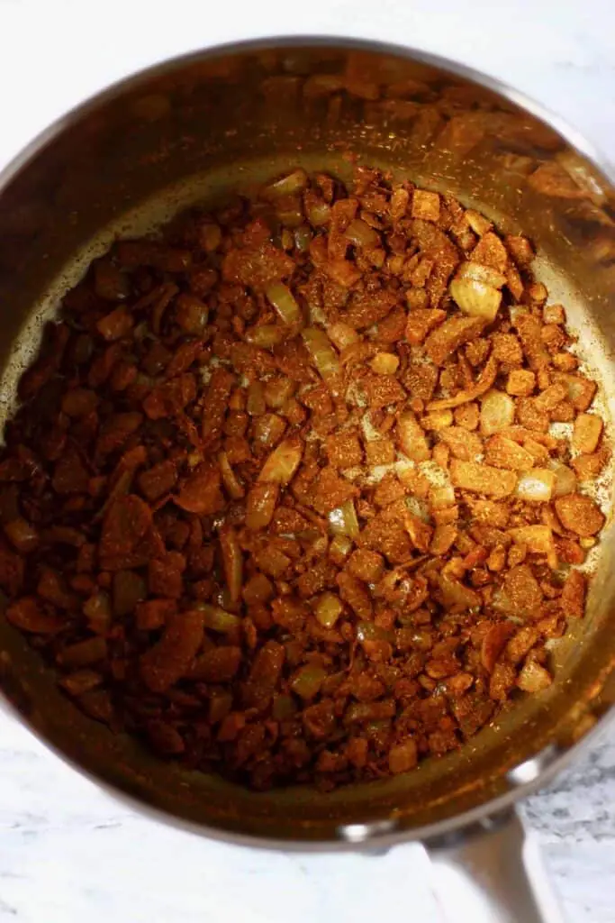 Photo of diced onion with brown spices being fried in a silver saucepan 
