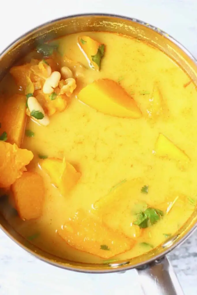 Photo of pumpkin, white beans and other vegetables being cooked in a yellow broth in a silver saucepan