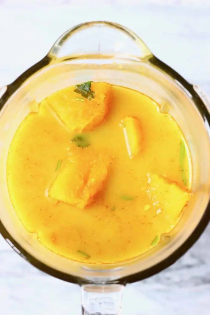 Photo of diced pumpkin and other vegetables in a yellow broth in a blender against a marble background