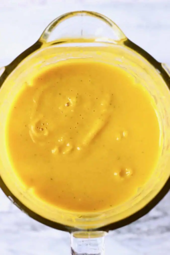 Photo of a bright yellow liquid in a blender against a marble background