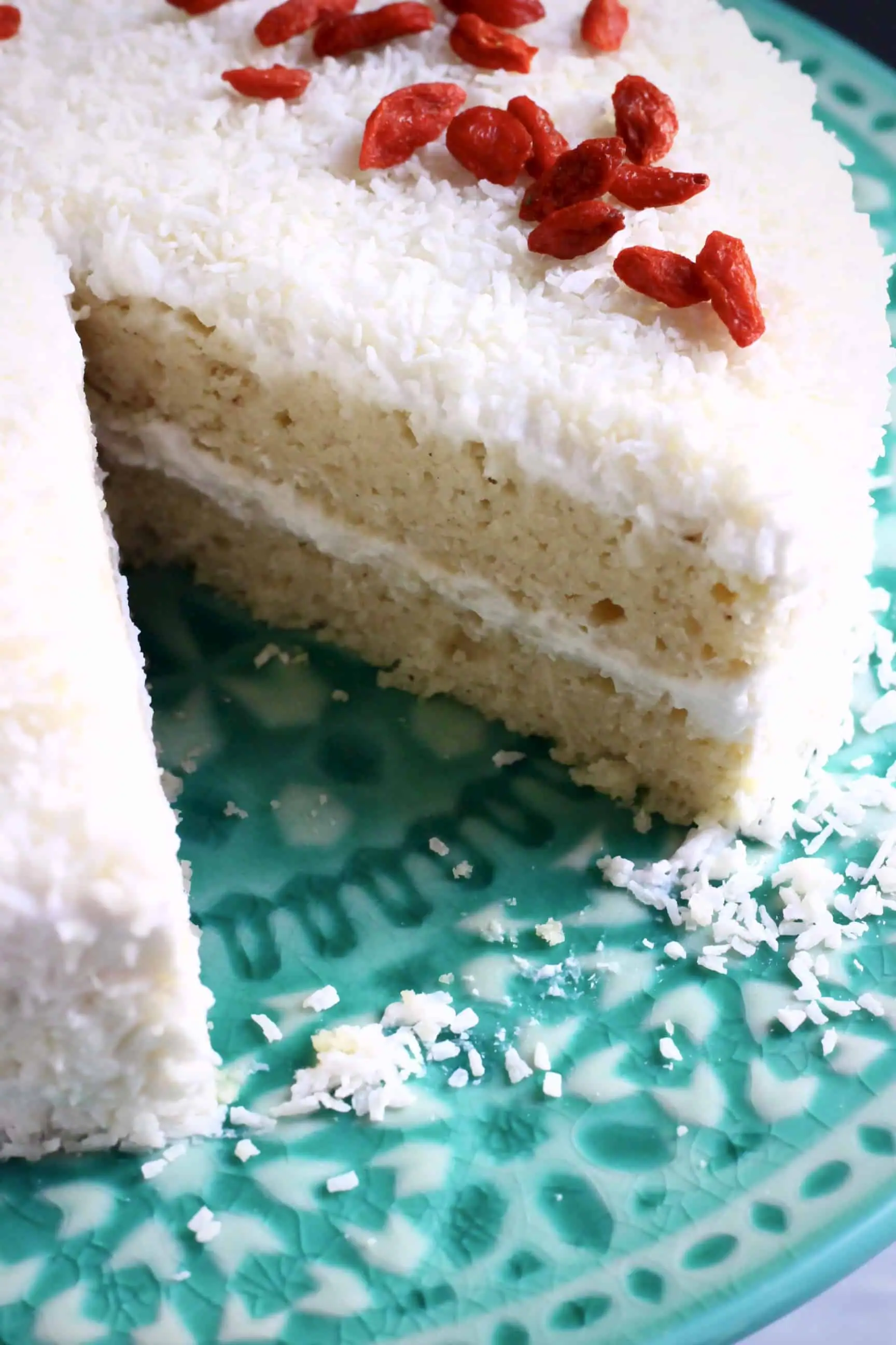 A sliced gluten-free vegan coconut sponge cake topped with desiccated coconut and red goji berries