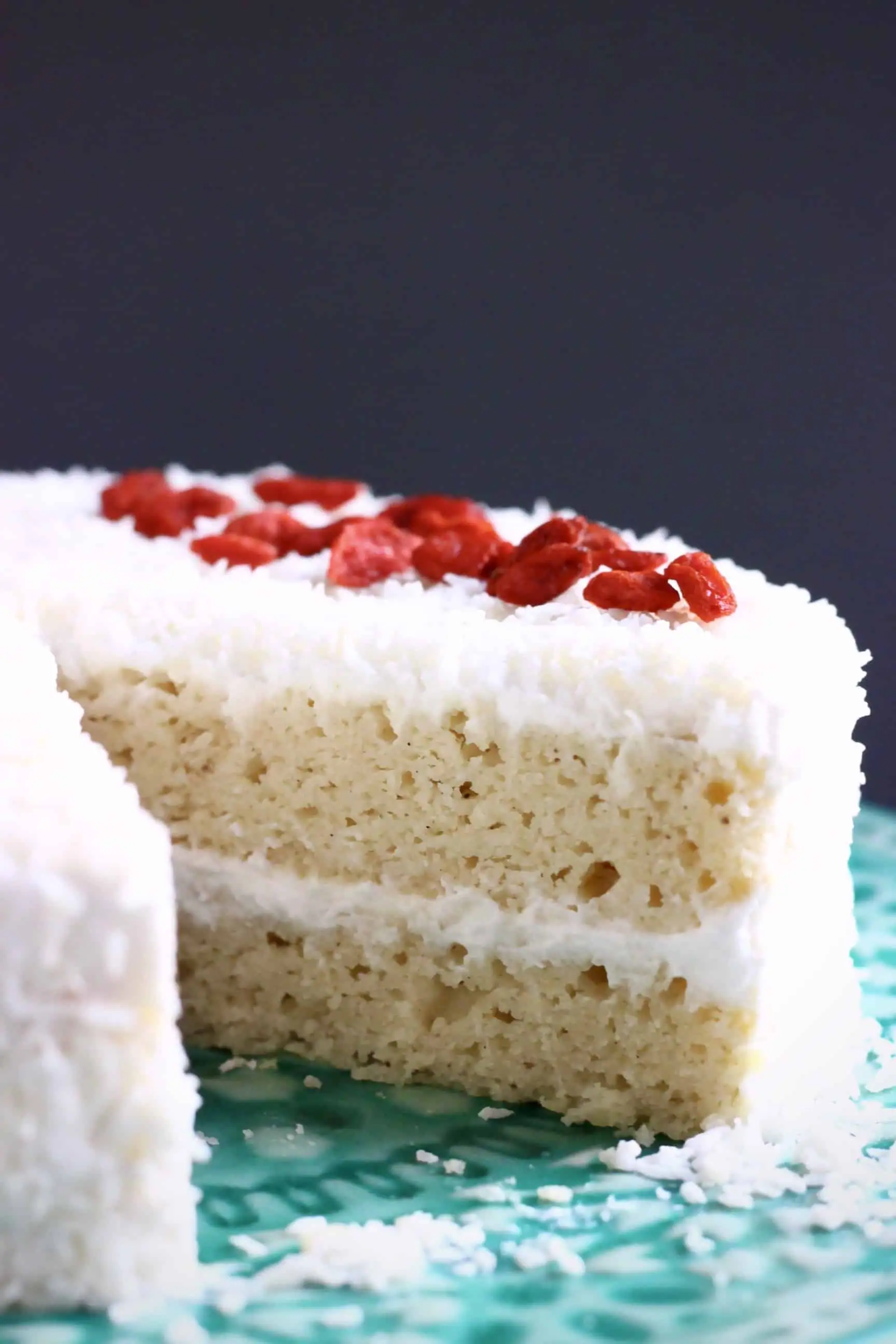 A sliced gluten-free vegan coconut cake topped with desiccated coconut and red goji berries