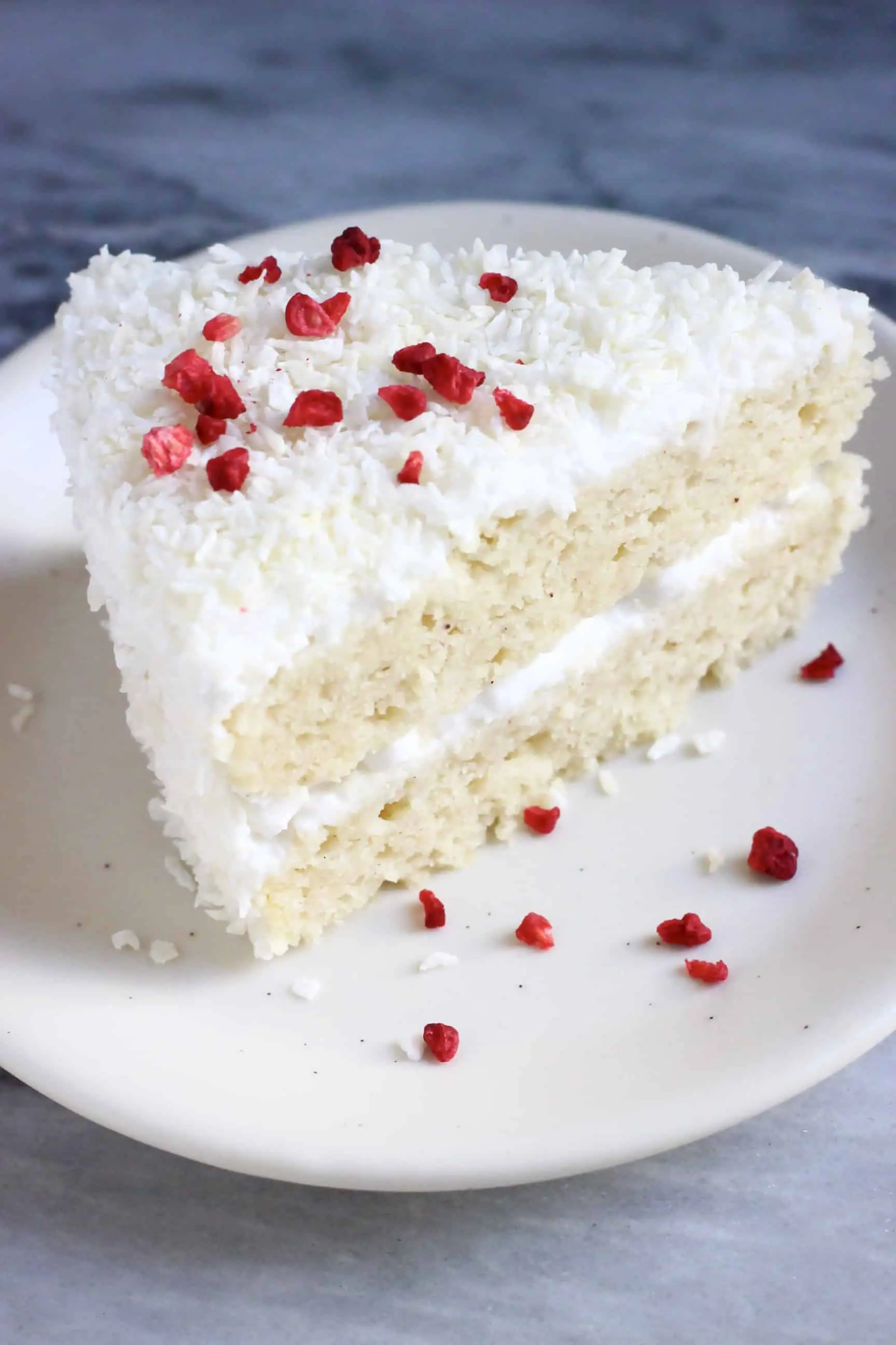A slice of gluten-free vegan coconut cake topped with desiccated coconut and freeze-dried raspberries