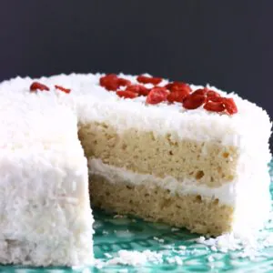 A sliced gluten-free vegan coconut cake topped with desiccated coconut and red goji berries