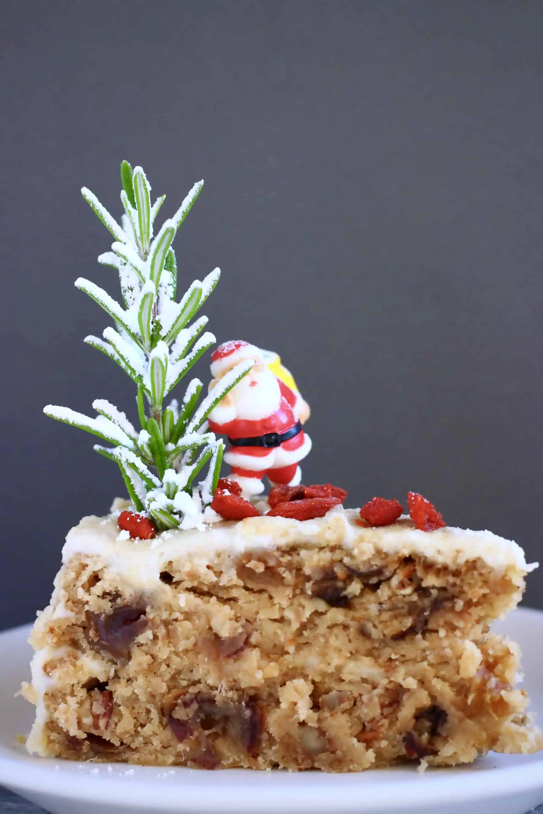 A slice of gluten-free vegan Christmas fruit cake covered in white buttercream topped with a plastic Santa 