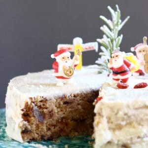A sliced gluten-free vegan Christmas fruit cake covered in white buttercream and decorated with Christmas decorations