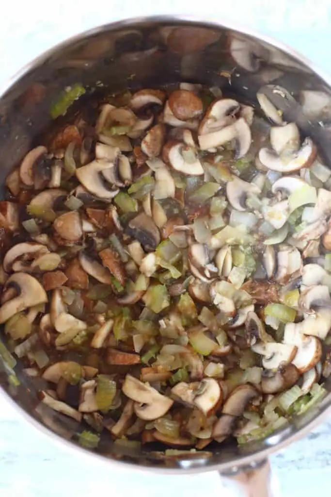 Diced onion, sliced celery and sliced mushrooms in a silver saucepan against a marble background