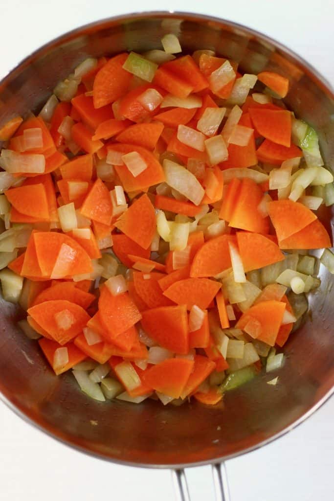 Onion, carrots, garlic and celery being fried in a silver pan