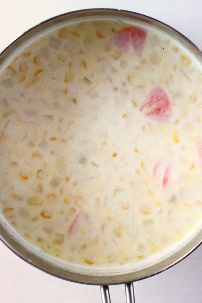 Sweetcorn, milk, white beans and vegetables in a silver saucepan against a white background